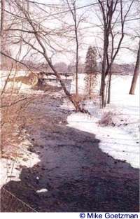 Snow borders the rippling water of a stream along Rustic Road 10