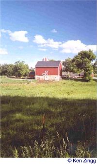 A red barn is caught between the blue of the sky and a verdant green pasture alongside Rustic Road 36